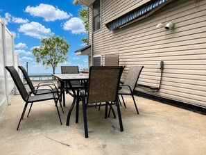 An outdoor patio with a table and chairs, a view of the ocean, and a building with siding and a security camera. - Sunset Oasis | Kayaks | Pedal Boat | Pier | Relax (Shipshewana)