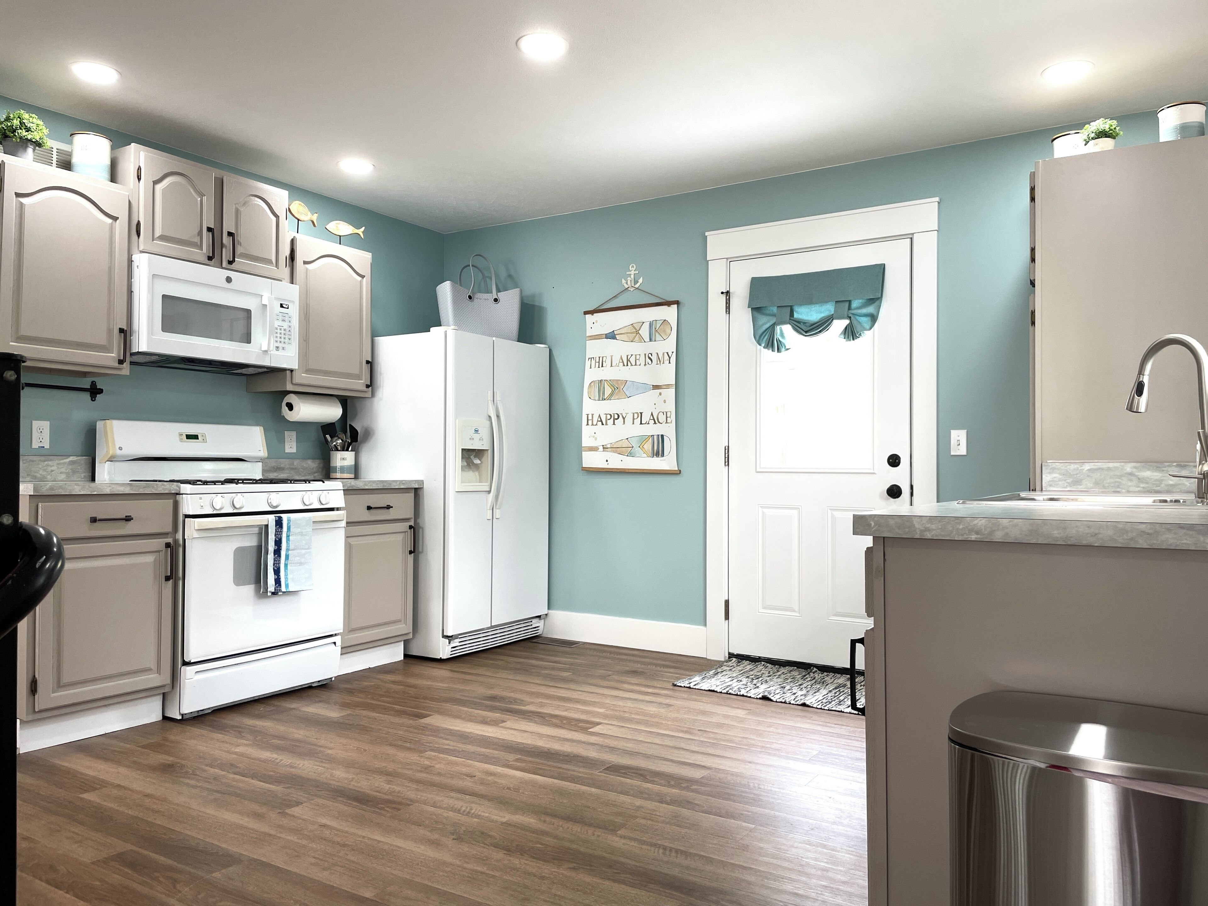 A kitchen with white appliances, a wooden floor, and a teal wall.
