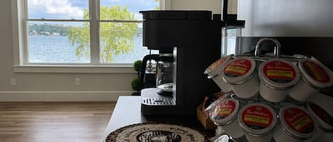 A kitchen with a coffee maker, a coffee mug rack, and a view of a lake through a window.