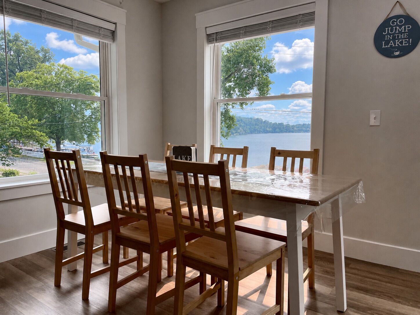 A dining area with a table and chairs, large windows with a view of a lake, and a sign on the wall.