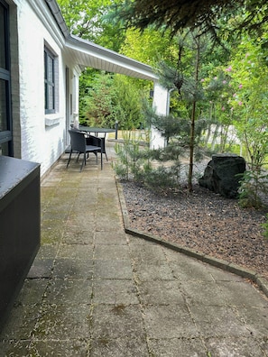 A patio area with a table and chairs, surrounded by a garden with various plants and a large rock. - Summer house by Limfjorden near Trend Strand (Løgstør)