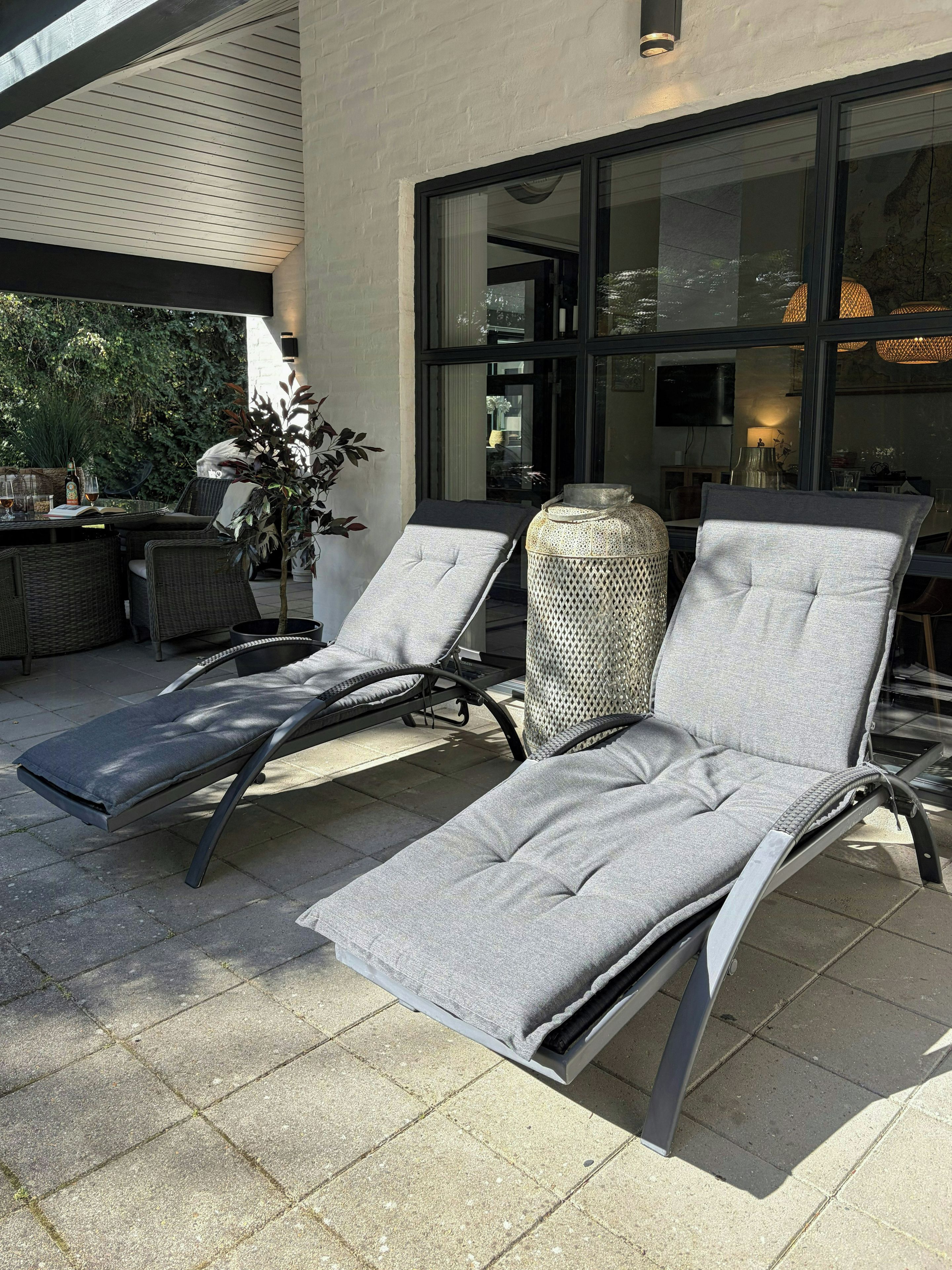 Eine Terrassenfläche mit zwei Liegestühlen, einem Blumentopf und einem Tisch mit Getränken.