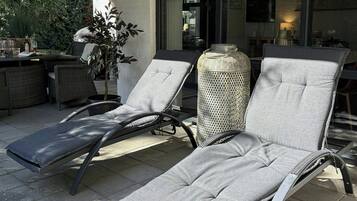 Eine Terrassenfläche mit zwei Liegestühlen, einem Blumentopf und einem Tisch mit Getränken.