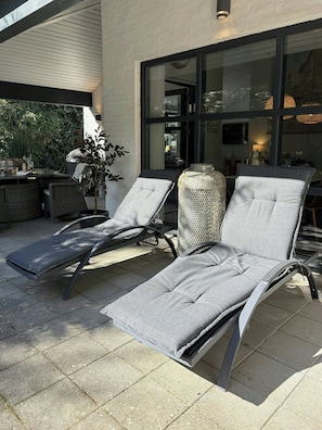 A patio area with two lounge chairs, a potted plant, and a table with drinks.