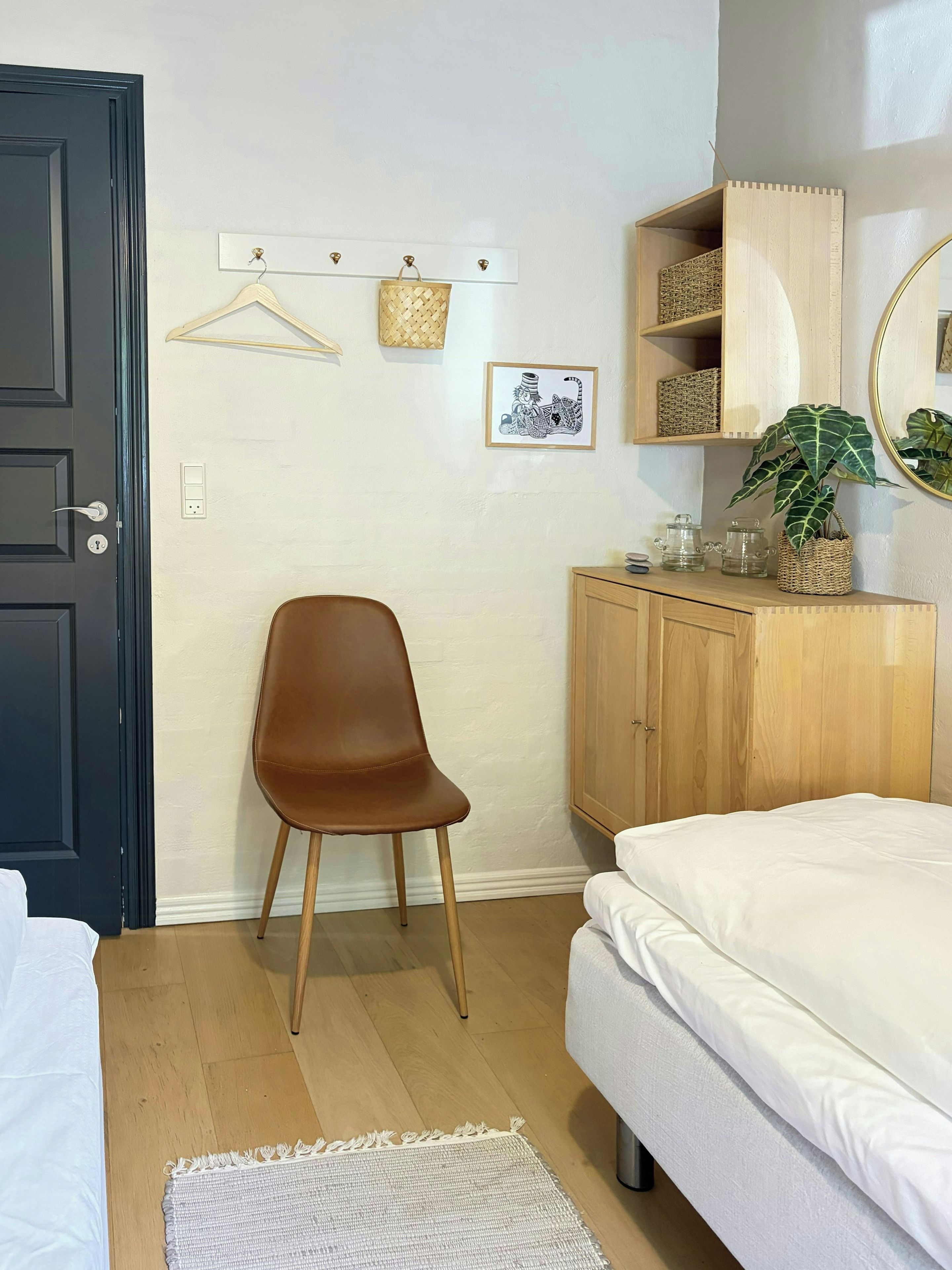 Un dormitorio con una cama, una silla, un armario, un perchero y un estante de pared con objetos decorativos.
