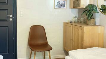 Un dormitorio con una cama, una silla, un armario, un perchero y un estante de pared con objetos decorativos.