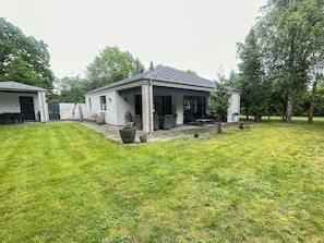A single-story house with a covered patio area, a lawn, and a tree in the foreground.