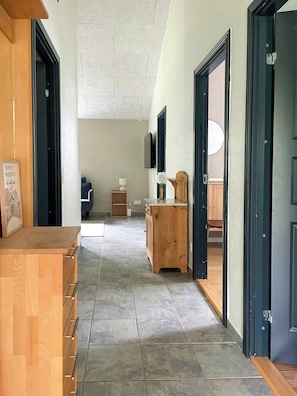 A hallway with a wooden cabinet, a television mounted on the wall, and a door leading to another room.