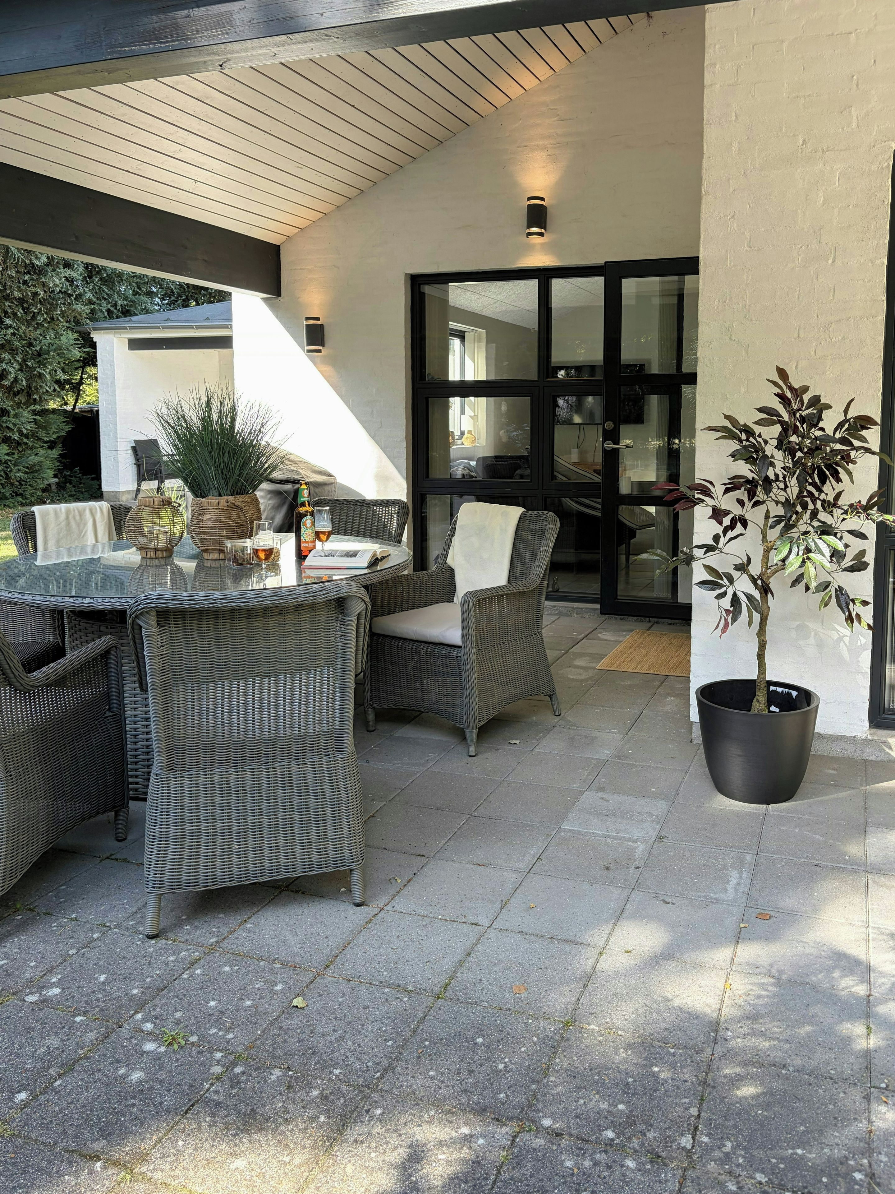 Ein möblierter Patio mit Korbmöbeln, einem Glastisch und einem Blumentopf.