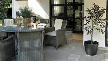 Ein möblierter Patio mit Korbmöbeln, einem Glastisch und einem Blumentopf.