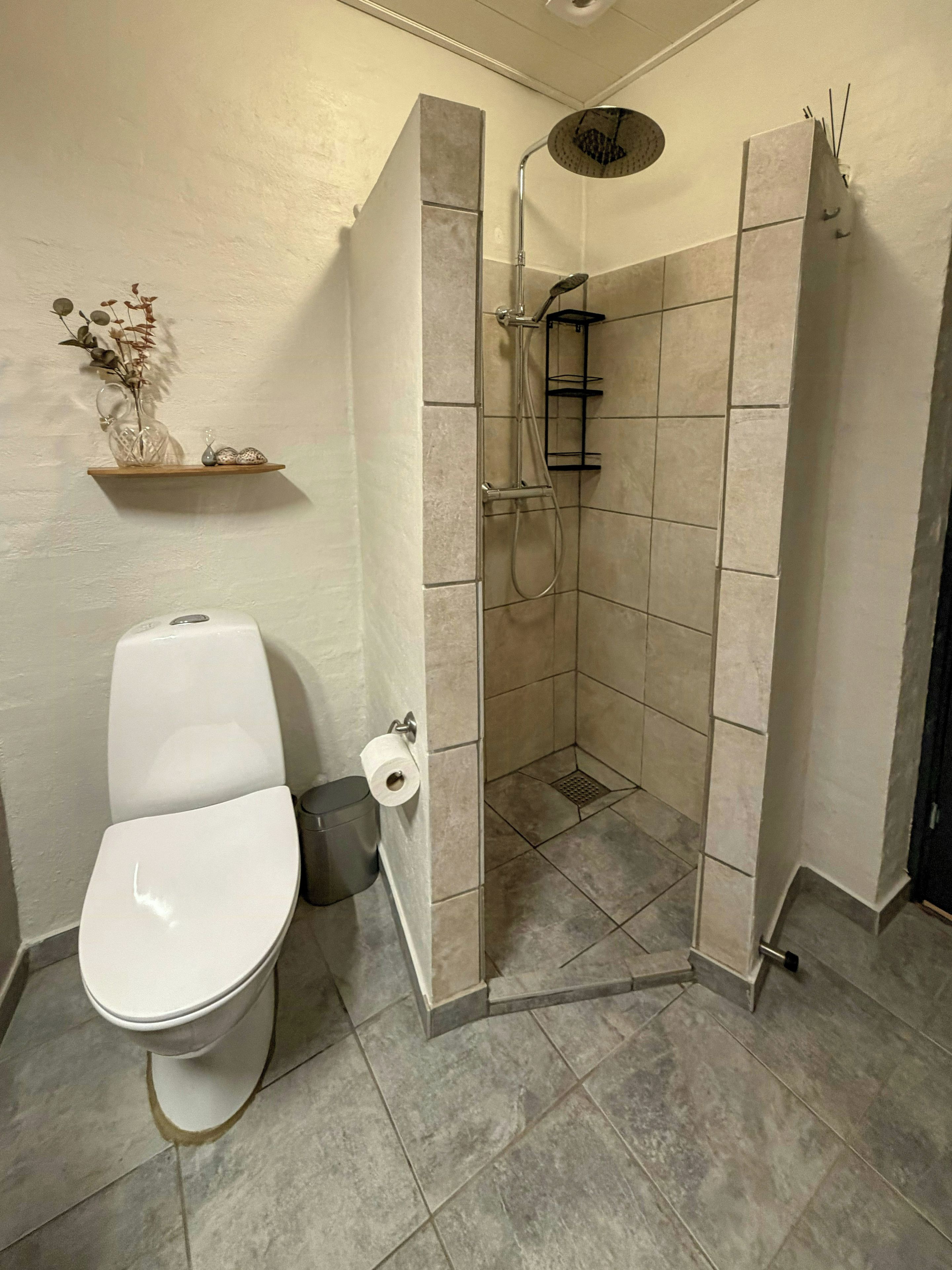 Un baño con inodoro, cabina de ducha y estante con adornos.