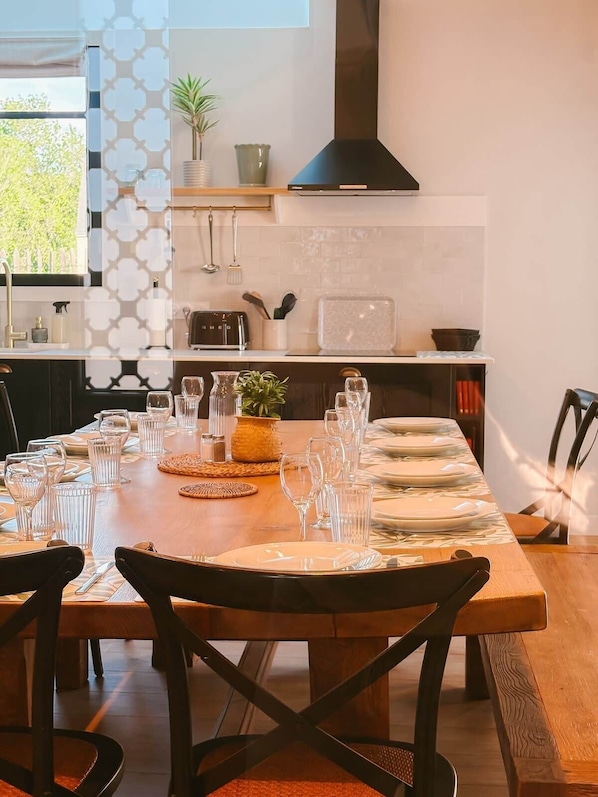 A dining area with a long table set for a meal, kitchenware, and a modern stove.