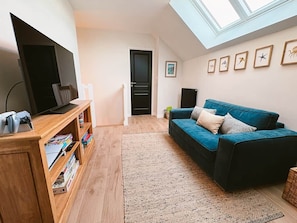 A living room with a TV, wooden entertainment unit, blue sofa, and a skylight.