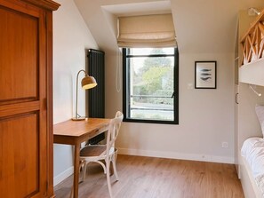 A bedroom with a bunk bed, a desk with a chair, a window with a view, and a framed picture on the wall. - Ker Paravel · Family villa · Beach 4 min · Garden (Saint-Lunaire)