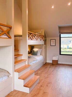 A bedroom with a bunk bed, wooden staircase, and a window with a view.