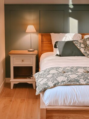 A bedroom with a wooden headboard, a bedside table with a lamp, and a floral-patterned bedspread.