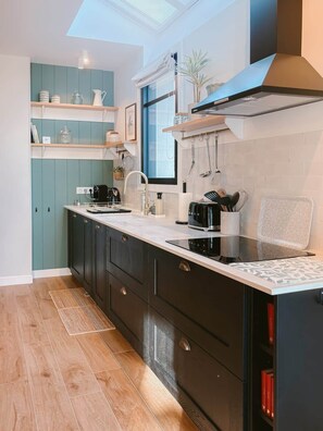 A modern kitchen with dark cabinetry, a white countertop, and a skylight above.