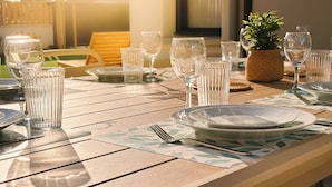 Ein sonniger Essbereich im Freien mit einem Tisch für zwei Personen, ausgestattet mit klarem Glas und Geschirr.