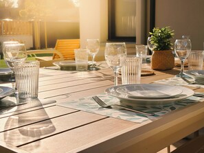 A sunlit outdoor dining area with a table set for two, featuring clear glassware and plates. - Ker Paravel · Family villa · Beach 4 min · Garden (Saint-Lunaire)