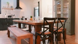Eine moderne Küche mit Esstisch, Stühlen und einer Bank. Es gibt einen Schrank mit Glastüren und eine Hängelampe.