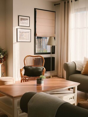 A living room with a wooden table, a wicker chair, a sofa, a floor lamp, and a window with curtains. - Ker Paravel · Family villa · Beach 4 min · Garden (Saint-Lunaire)