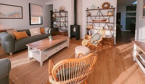 A living room with a sofa, coffee table, wicker chairs, a bookshelf, and a fireplace.