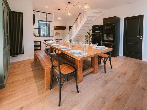 A dining area with a wooden table set for four, surrounded by chairs, in a modern kitchen with a staircase and black cabinetry.