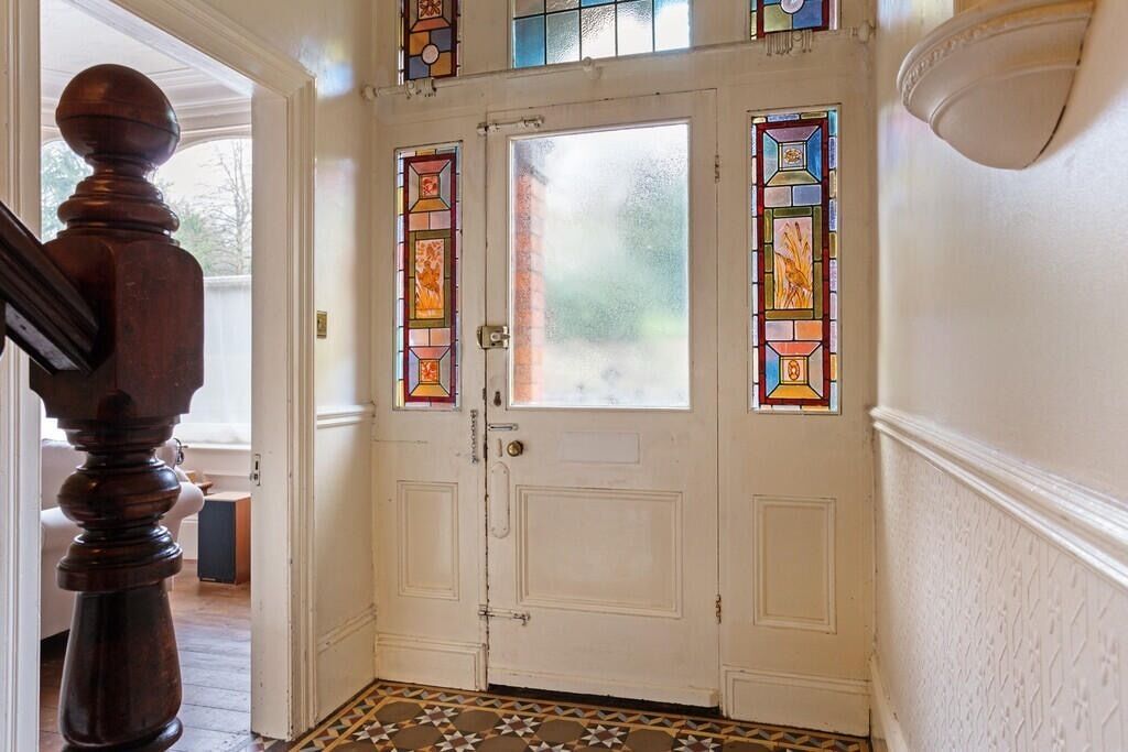 A white door with stained glass panels and a wooden staircase to the left.