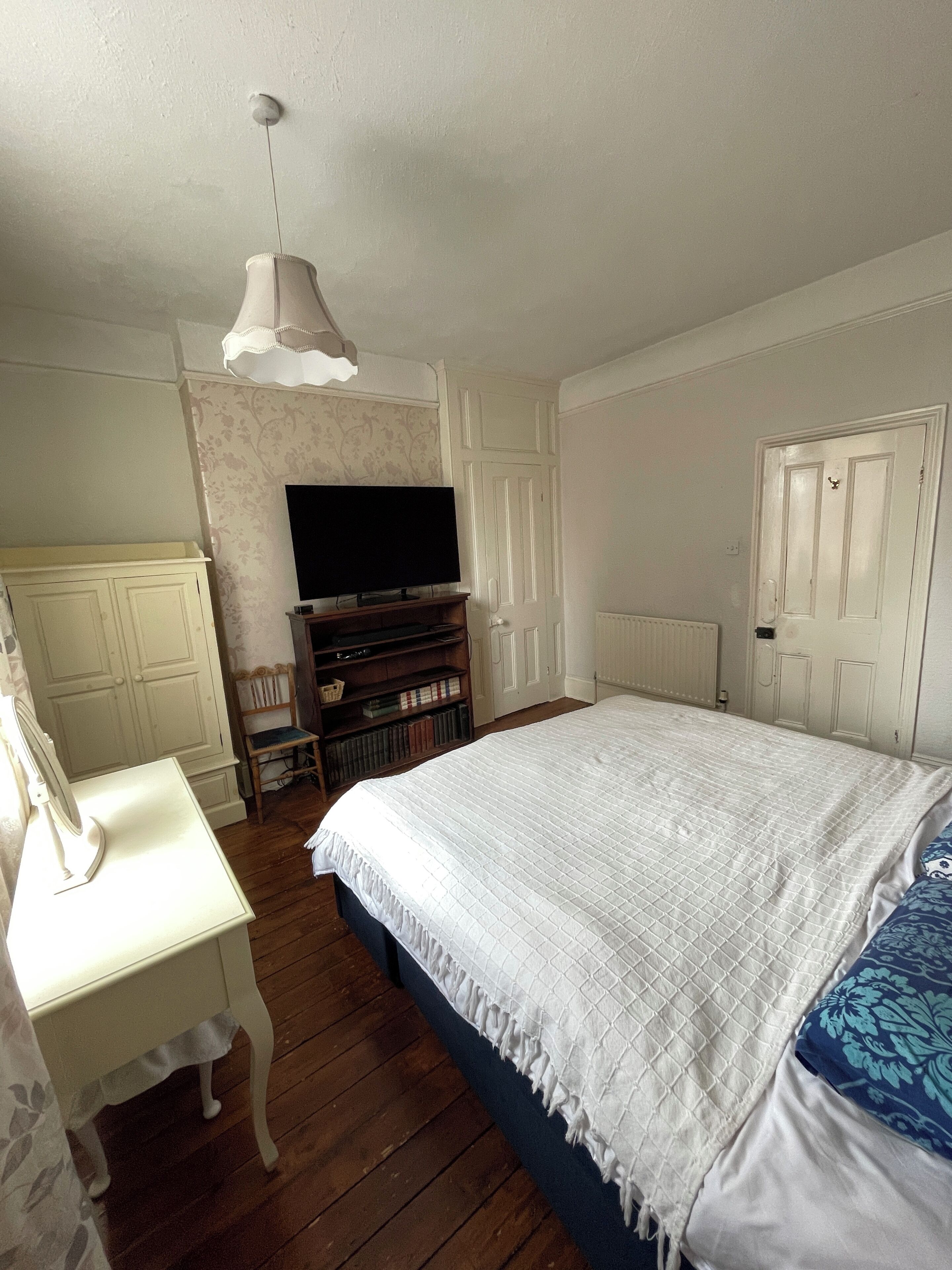 A bedroom with a large bed, a television on a stand, a desk, and a chair.