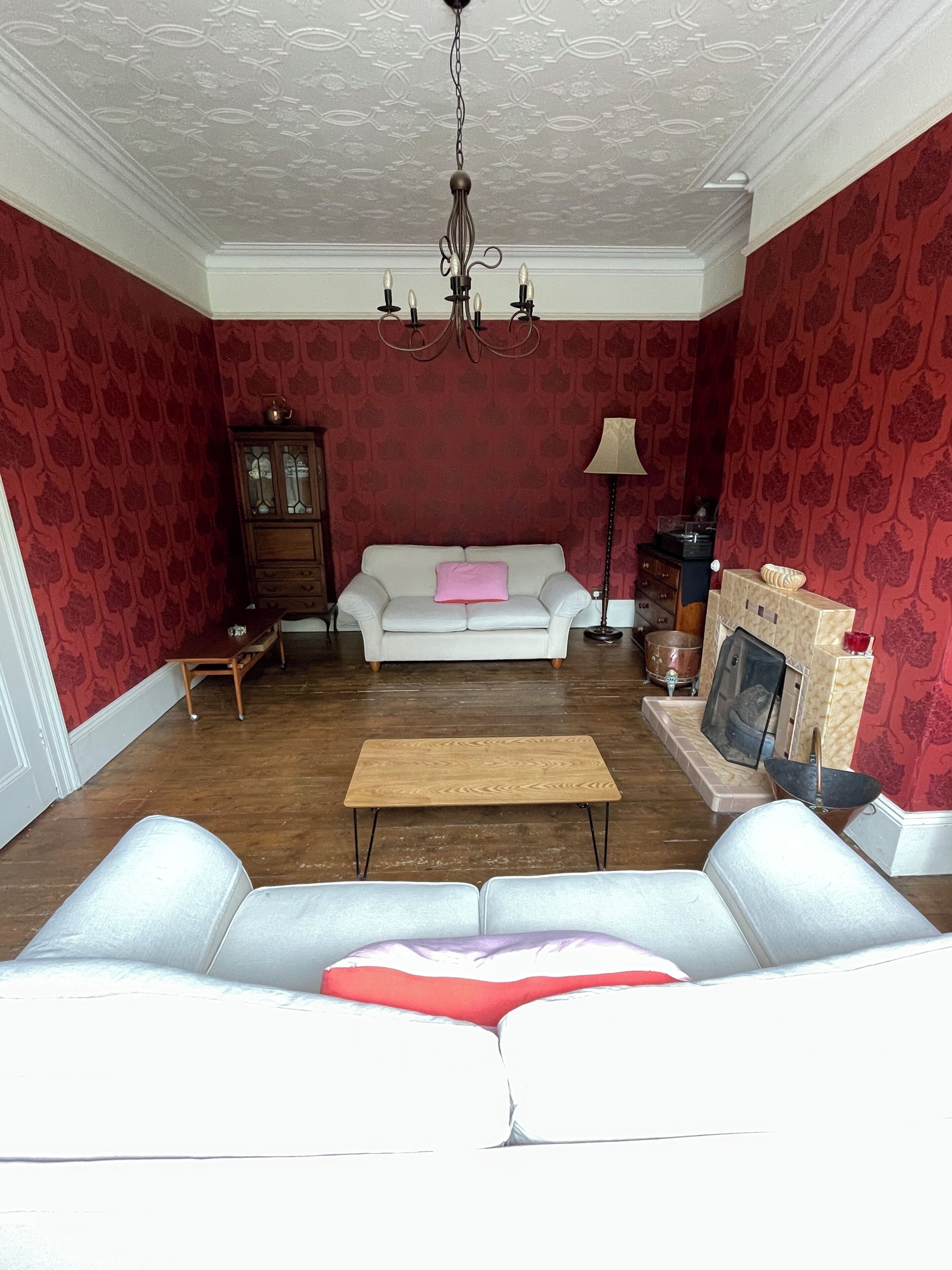 Ein Wohnzimmer mit einem weißen Sofa, einem Holztisch, einer Kristallleuchter, einem Schrank und Wandpapier mit Muster.