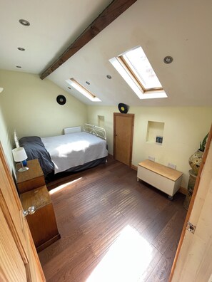 A bedroom with a bed, a bedside table, a wooden bench, a radiator, a door, and a skylight.