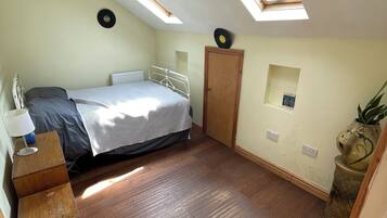 Een slaapkamer met een bed, dakramen, een houten dressoir en een klein plankje met een vaas.