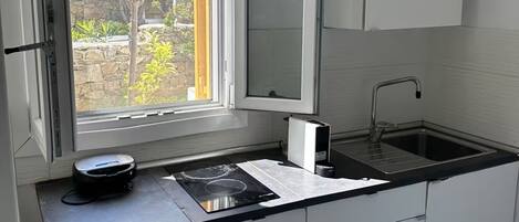 A modern kitchen with a built-in stove, a sink, and a window with a view of greenery.