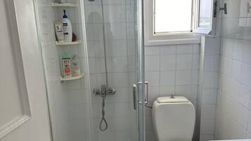 A bathroom with a glass-enclosed shower, a toilet, and a window above the sink.