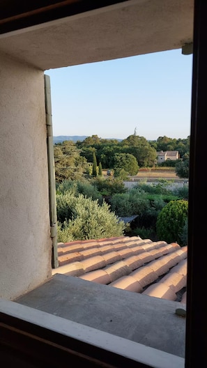 A view from a window with a concrete balcony edge, overlooking a landscape with trees and a distant building. - A House Nestled Among Olive Trees • Luberon • Village a 5-minute walk away (Saint-Saturnin-lès-Apt)