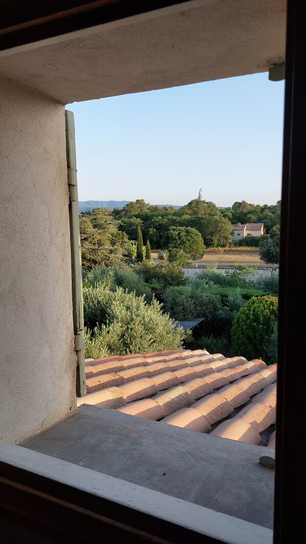 A view from a window with a concrete balcony edge, overlooking a landscape with trees and a distant building.