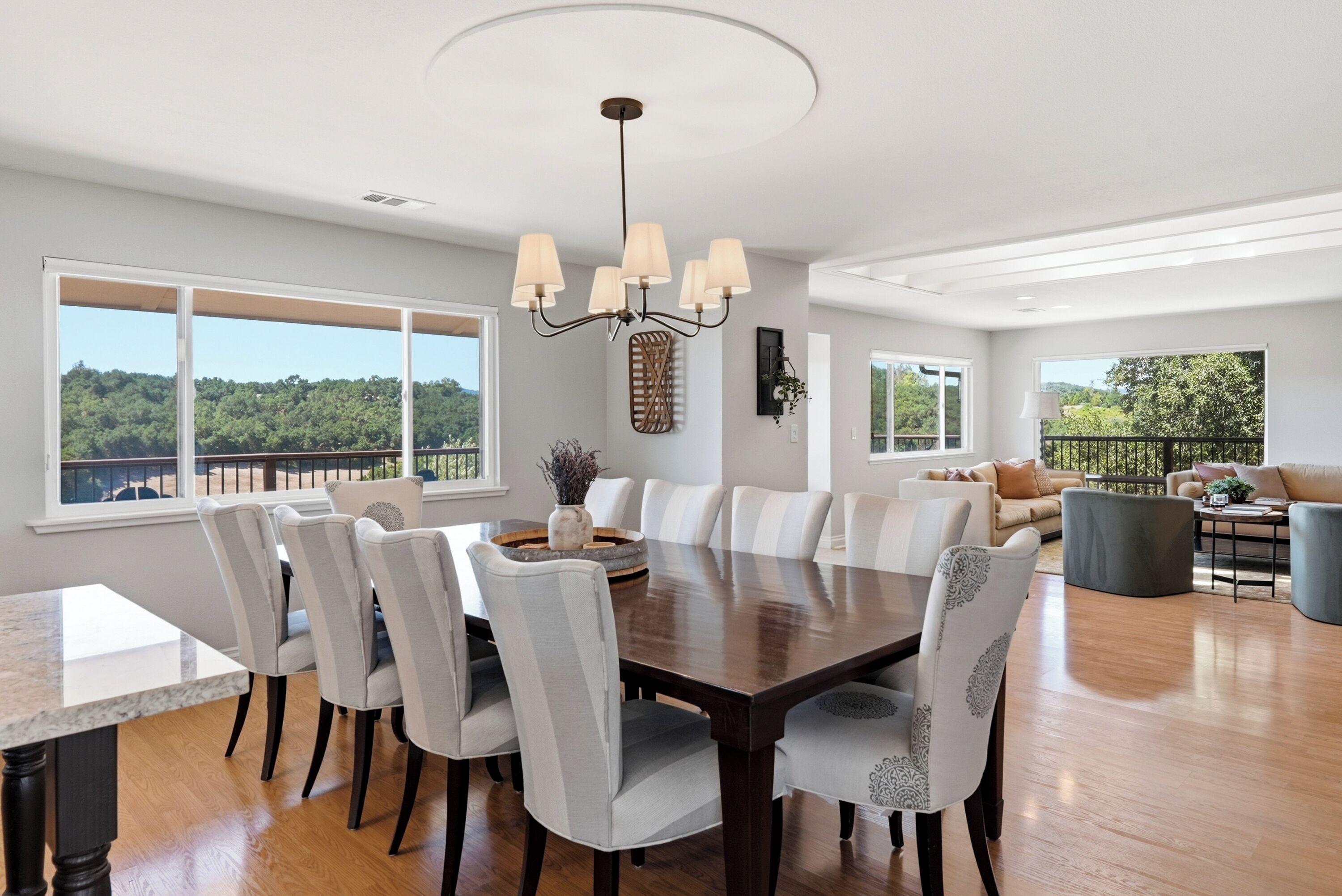 A spacious dining area with a large table and chairs, a chandelier, and large windows offering a view of the outdoors.