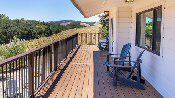 Un terrazzo in legno con ringhiera, due sedie e un tavolo.