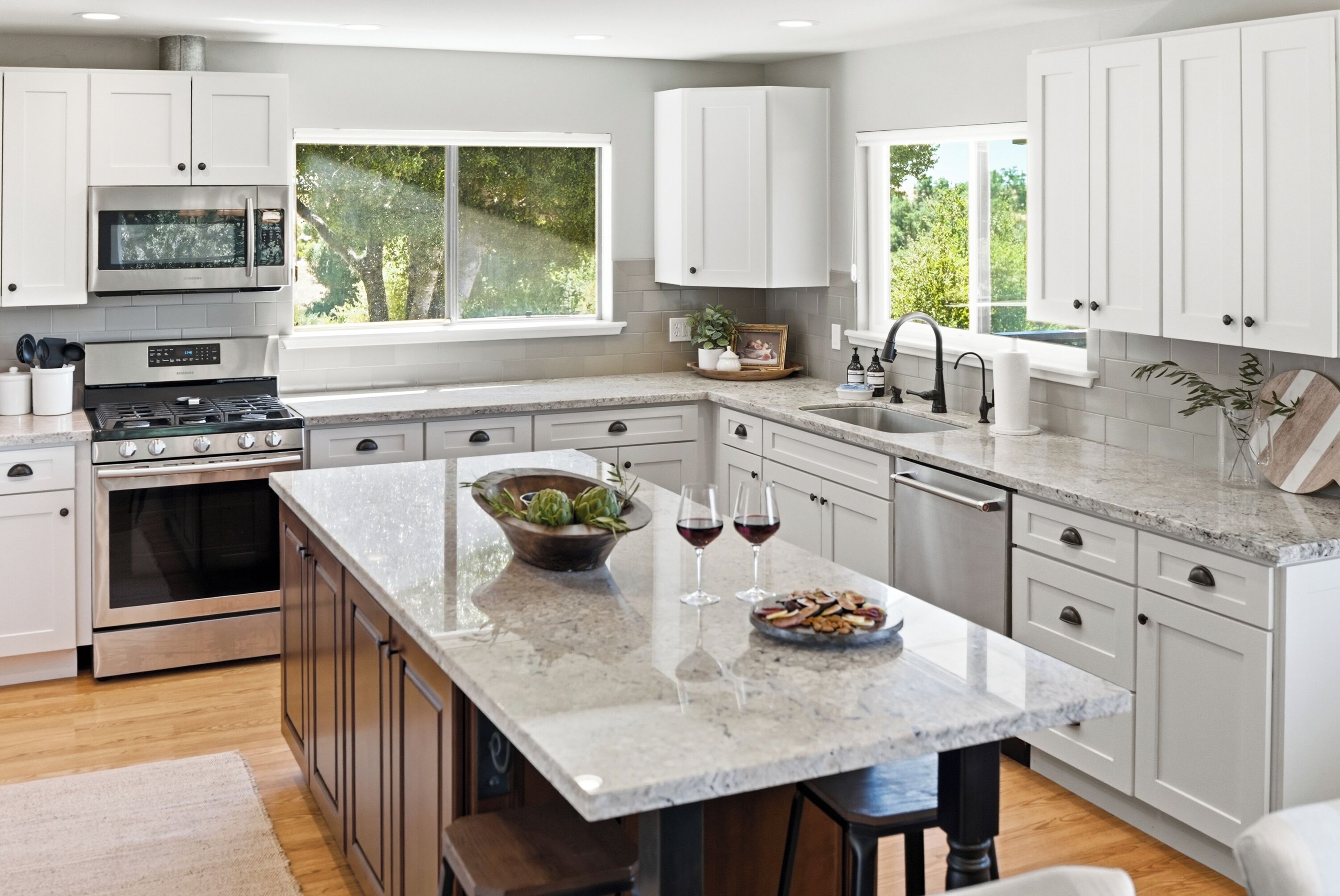 A modern kitchen with white cabinets, a central island, a built-in oven, and a window providing a view of greenery.