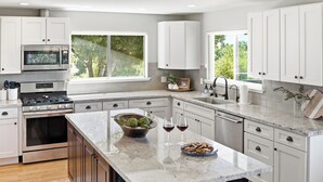 Una cucina moderna con mobili bianchi, un'isola centrale, forno integrato e una finestra che offre vista sul verde.