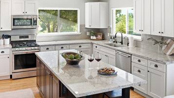 A modern kitchen with white cabinets, a central island, a built-in oven, and a window providing a view of greenery.