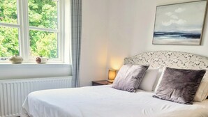 A neatly made bed with a headboard, a window with curtains, a radiator, and a painting on the wall. - 2 Bed House - Sleeps 4 - Pets - Parking - Beach (Cromarty)