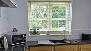 A modern kitchen with wooden cabinets, a microwave, a kettle, and a window with blinds. - 2 Bed House - Sleeps 4 - Pets - Parking - Beach (Cromarty)
