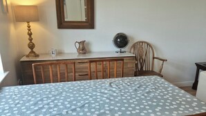 A dining area with a table covered in a polka dot tablecloth, wooden chairs, a lamp, a mirror, and a pitcher on a cabinet. - 2 Bed House - Sleeps 4 - Pets - Parking - Beach (Cromarty)