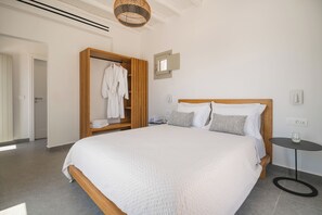 A modern bedroom with a large bed, a wooden wardrobe, and a small table. - Vrachos Retreats Sunset Sea View Villa - 3BR (Mykonos)