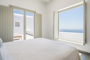 Een slaapkamer met een bed, een bankje en een groot raam met uitzicht op zee.