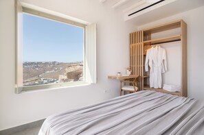 Een hotelkamer met een bed, een houten kast, een bureau en een groot raam met uitzicht op een landschap.