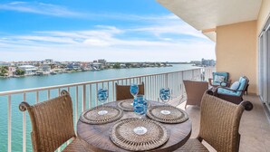 Ein Balkon mit Korbmöbeln, einem Tisch mit dekorativem Glas und Blick auf einen Fluss sowie die Skyline einer Stadt.