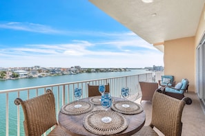 Ein Balkon mit Korbmöbeln, einem Tisch mit dekorativem Glas und Blick auf einen Fluss sowie die Skyline einer Stadt.