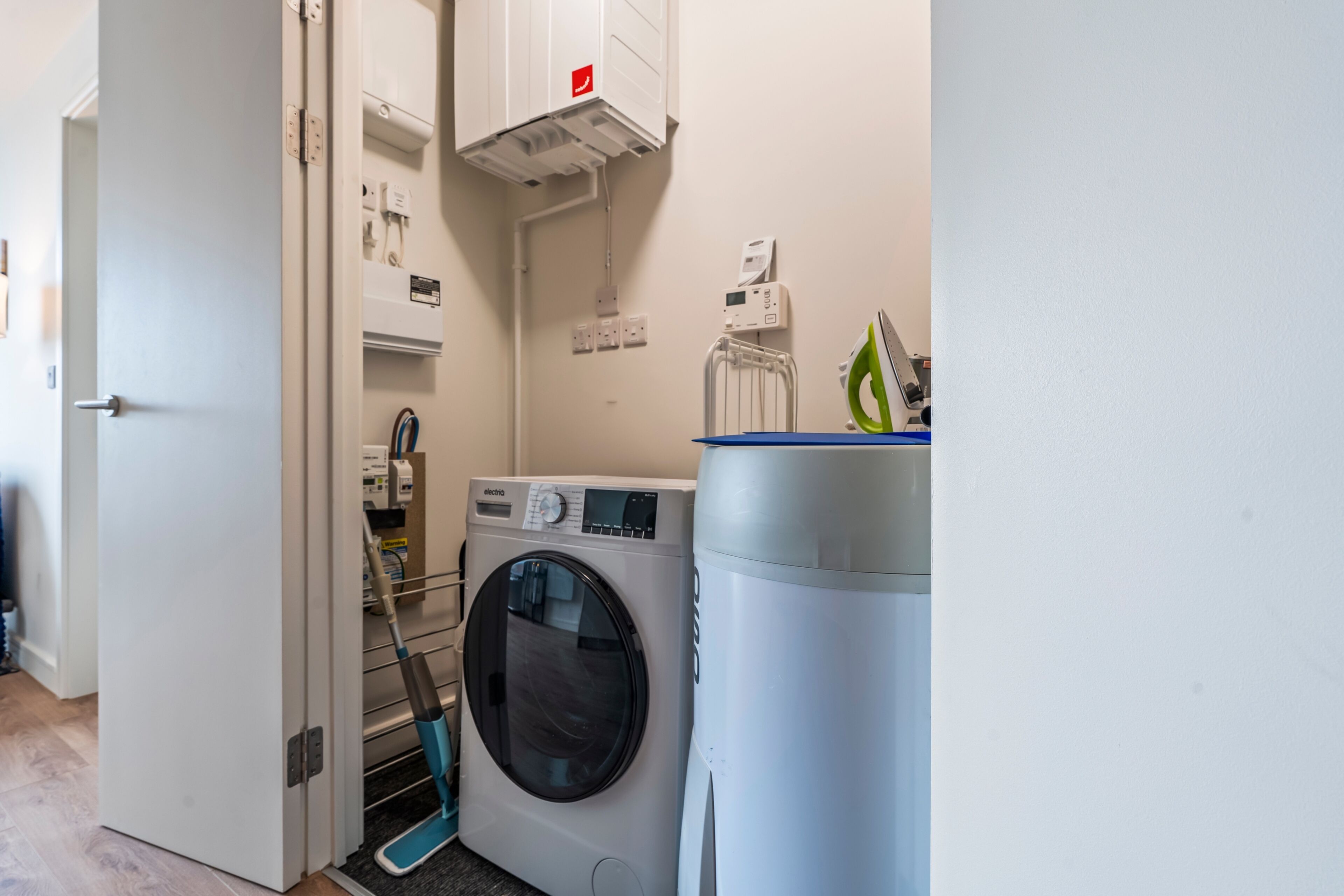 A laundry room with a front-loading washing machine, a drying rack, and a large water tank.